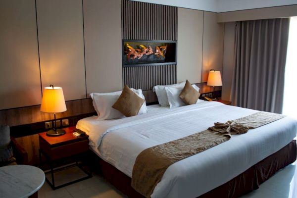 A cozy hotel room features a large bed with pillows, warm lighting from bedside lamps, elegant decor, and a window with curtains.