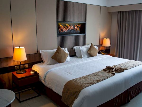 A cozy hotel room features a large bed with pillows, warm lighting from bedside lamps, elegant decor, and a window with curtains.