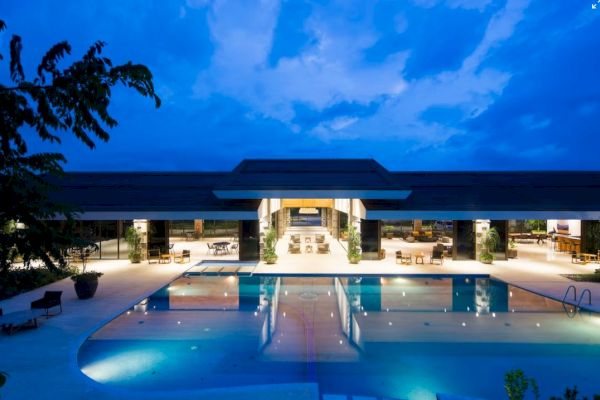 A luxurious building is illuminated at dusk, featuring an inviting swimming pool and open seating areas, creating a serene atmosphere.