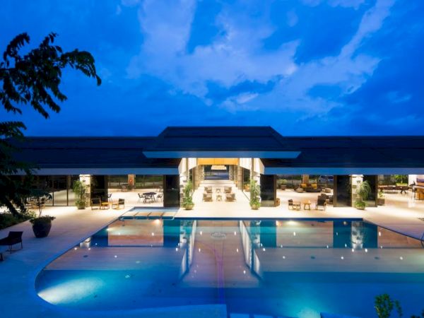 A luxurious building is illuminated at dusk, featuring an inviting swimming pool and open seating areas, creating a serene atmosphere.