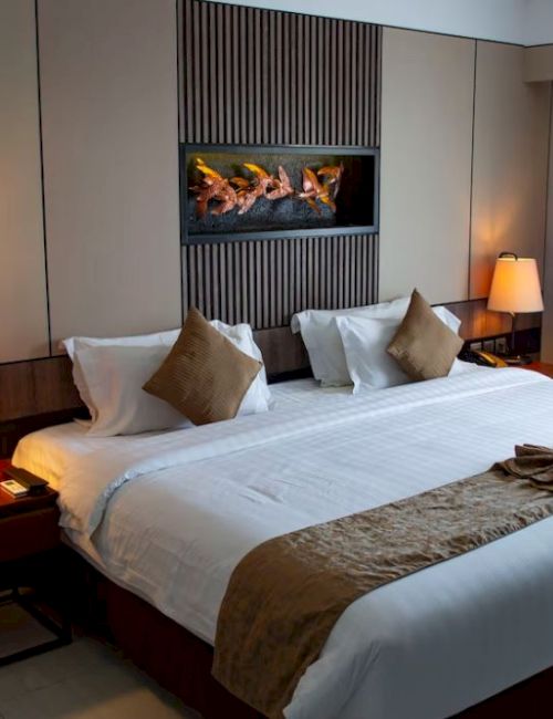 A cozy hotel room with a large bed, elegant lamps, and a decorative wall feature. The room has a modern and inviting atmosphere.