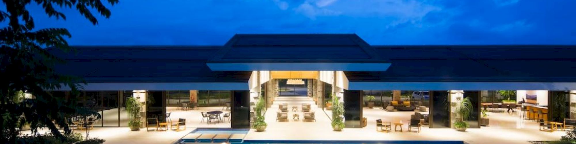 A modern building with large glass windows is illuminated at night, featuring a symmetrical, reflective pool in front of it.