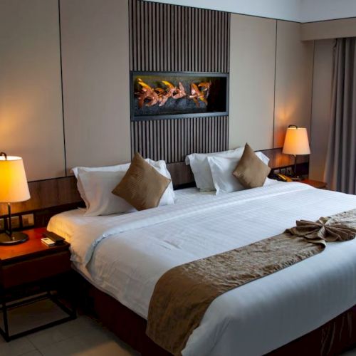 A neatly arranged hotel room with a large bed, cozy lighting from lamps, and a modern wall-mounted decoration.