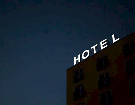 A building exterior with a partially lit sign reading "HOTEL" against a dark sky, with some windows visible.