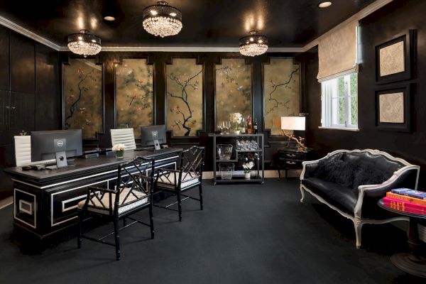 A stylish office with a black desk, three chairs, computers, floral artwork, elegant sofas, and a drink cart.