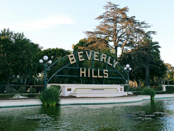 The image shows the iconic Beverly Hills sign with surrounding greenery and a pond in front of it.