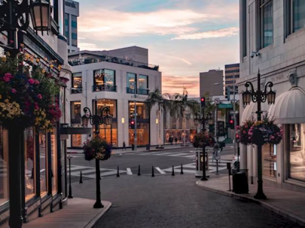 A quiet urban street with elegant buildings and flowered lampposts under a colorful sunset sky.