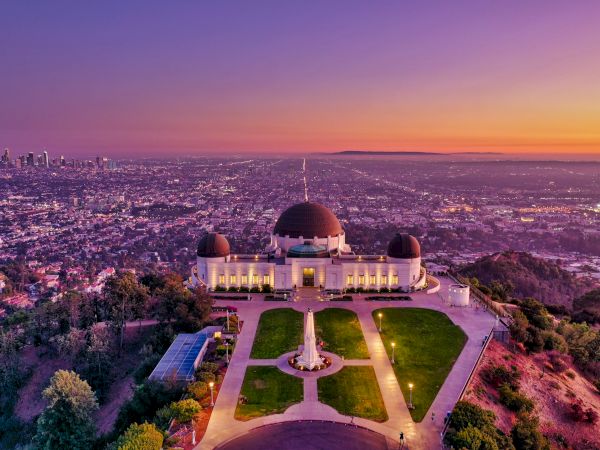 The image shows the Griffith Observatory at sunset, overlooking Los Angeles with the cityscape and sky displaying vibrant colors.