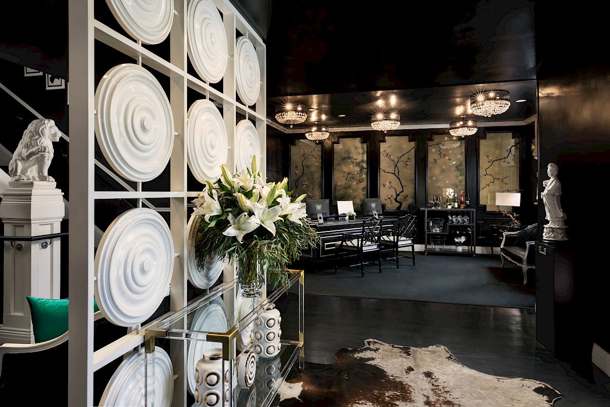 A stylish interior with decorative white panels, elegant lighting, statues, and a table with chairs, all set on a dark floor with a rug.