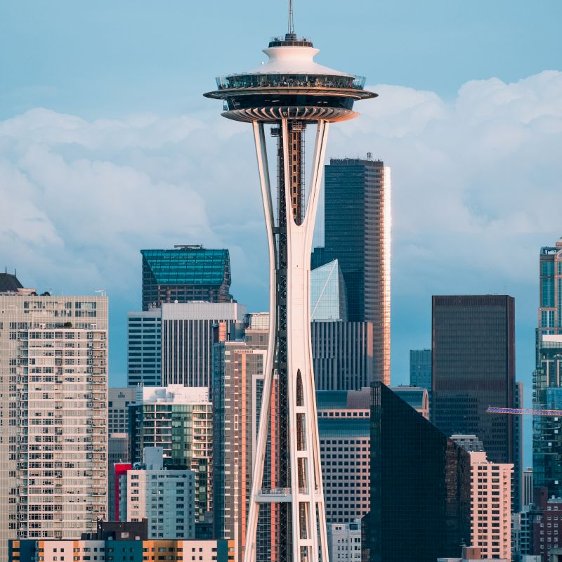 The image shows the Space Needle in Seattle amid a backdrop of modern skyscrapers and cloudy skies.