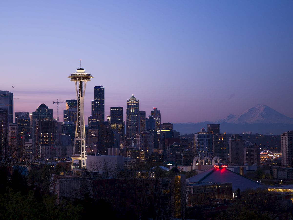 Seattle skyline at dusk with the Space Needle and Mount Rainier in the background, under a twilight sky.