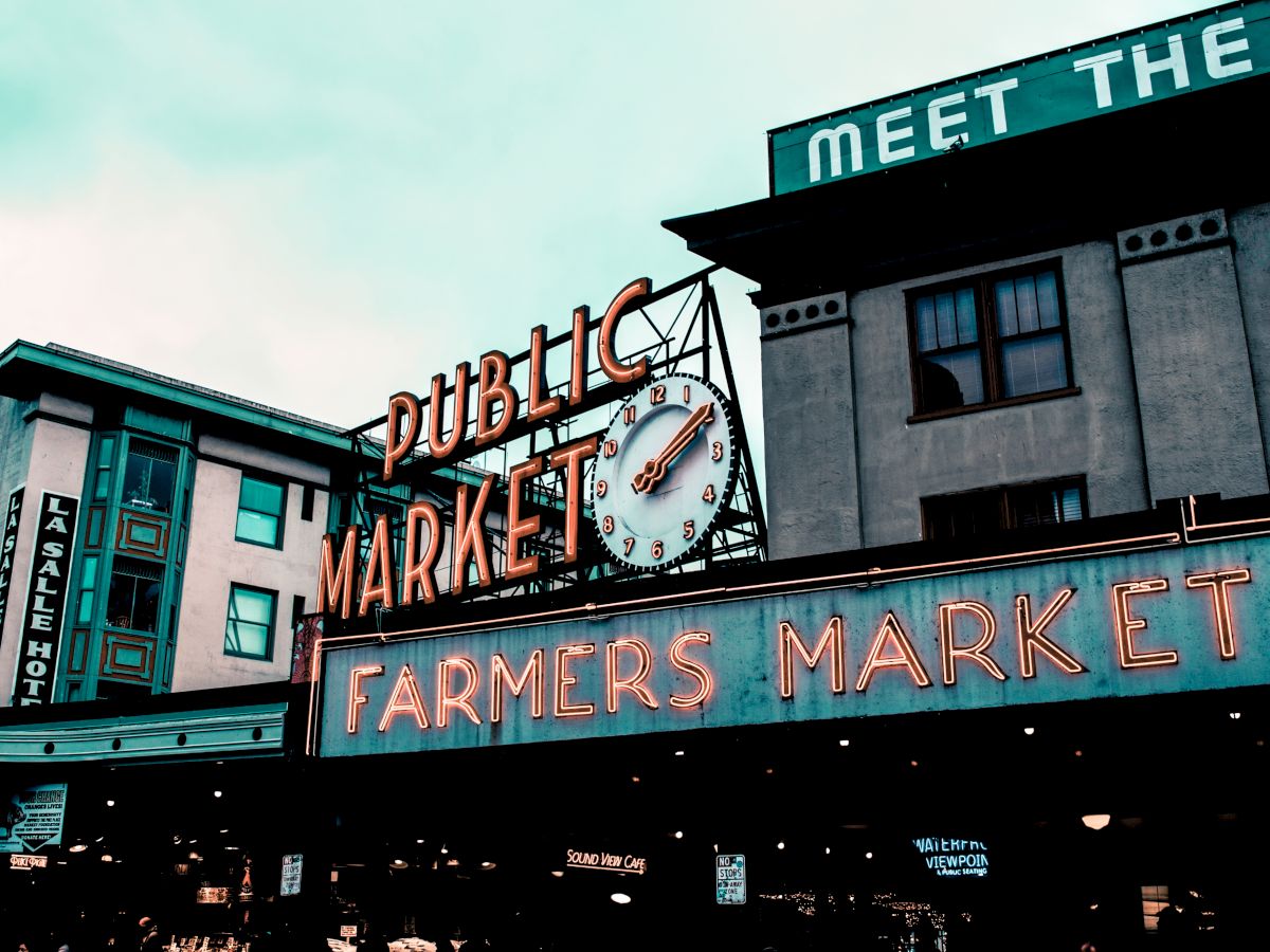 The image shows a famous public farmers market with retro neon signs and a clock.