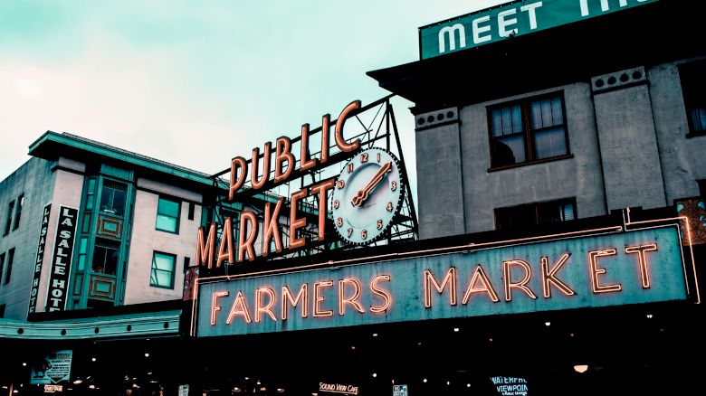 The image shows a famous public farmers market with retro neon signs and a clock.