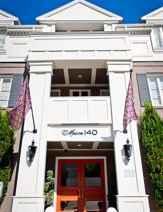 Maison 140 grand exterior featuring large orange doors, decorative flags, and large white pillars.
